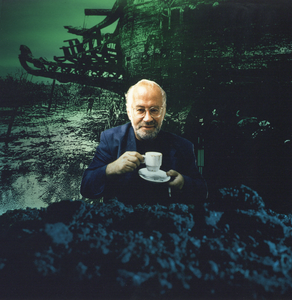 360023 Portret van filmmaker en horecaondernemer Jos Stelling, met een kopje koffie in een decor van zijn film De ...